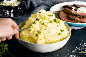 Creamy garlic mashed potatoes piled high in a bowl with chives on top, taking a spoonful