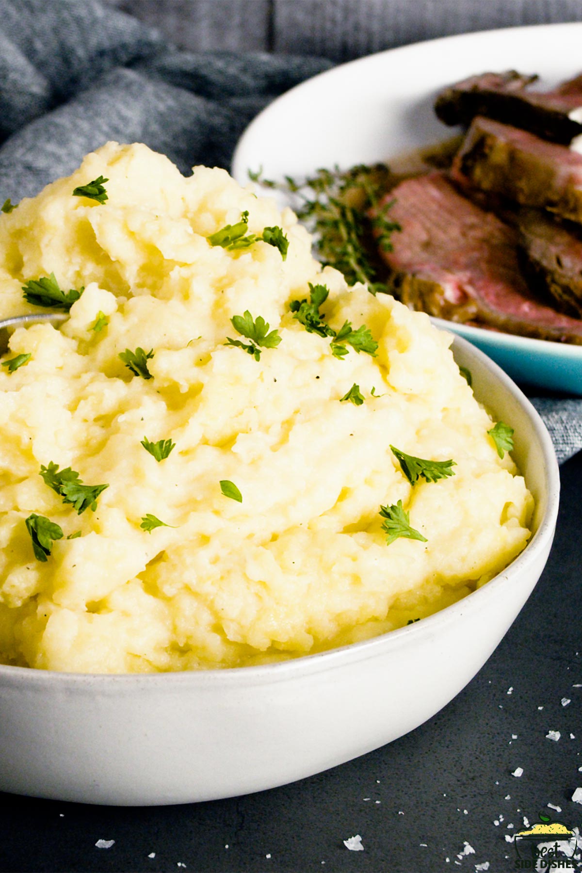 Creamy garlic mashed potatoes piled in a bowl with chives, next to roast beef