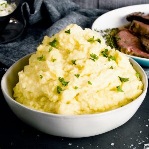 Creamy garlic mashed potatoes piled high in a bowl with chives on top
