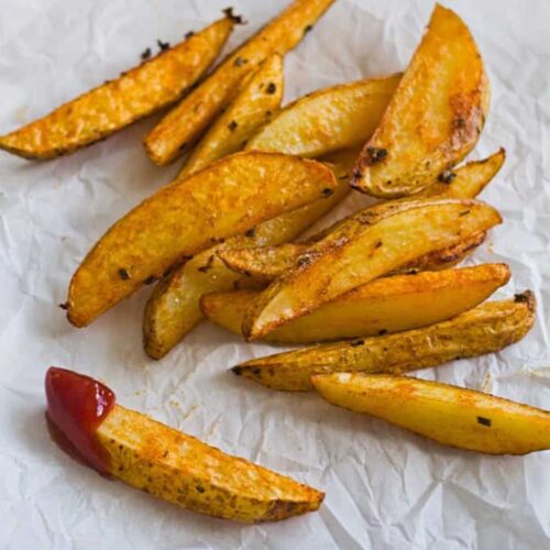 crispy baked potato wedges on parchment paper, one dipped in ketchup