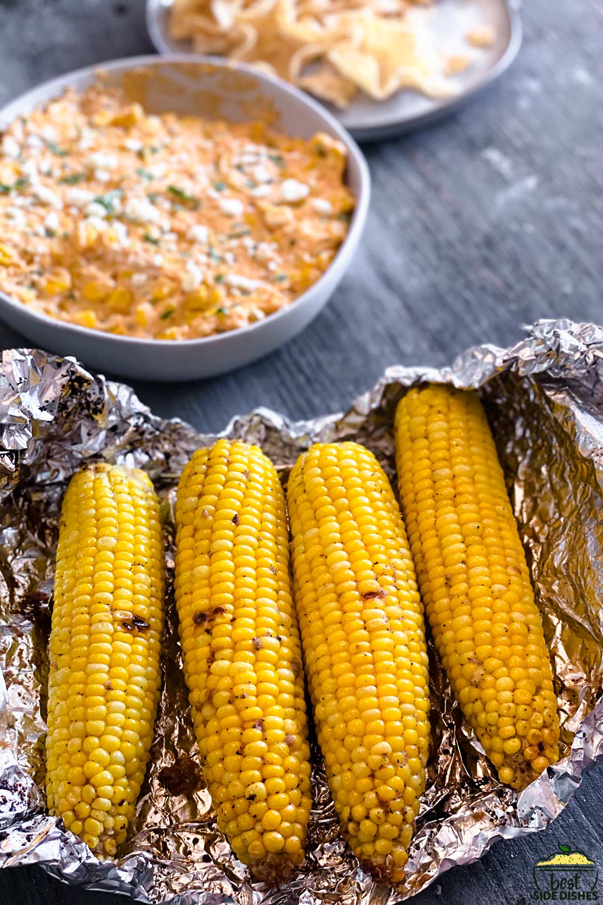 grilled corn on the cob in foil next to corn dip in a bowl