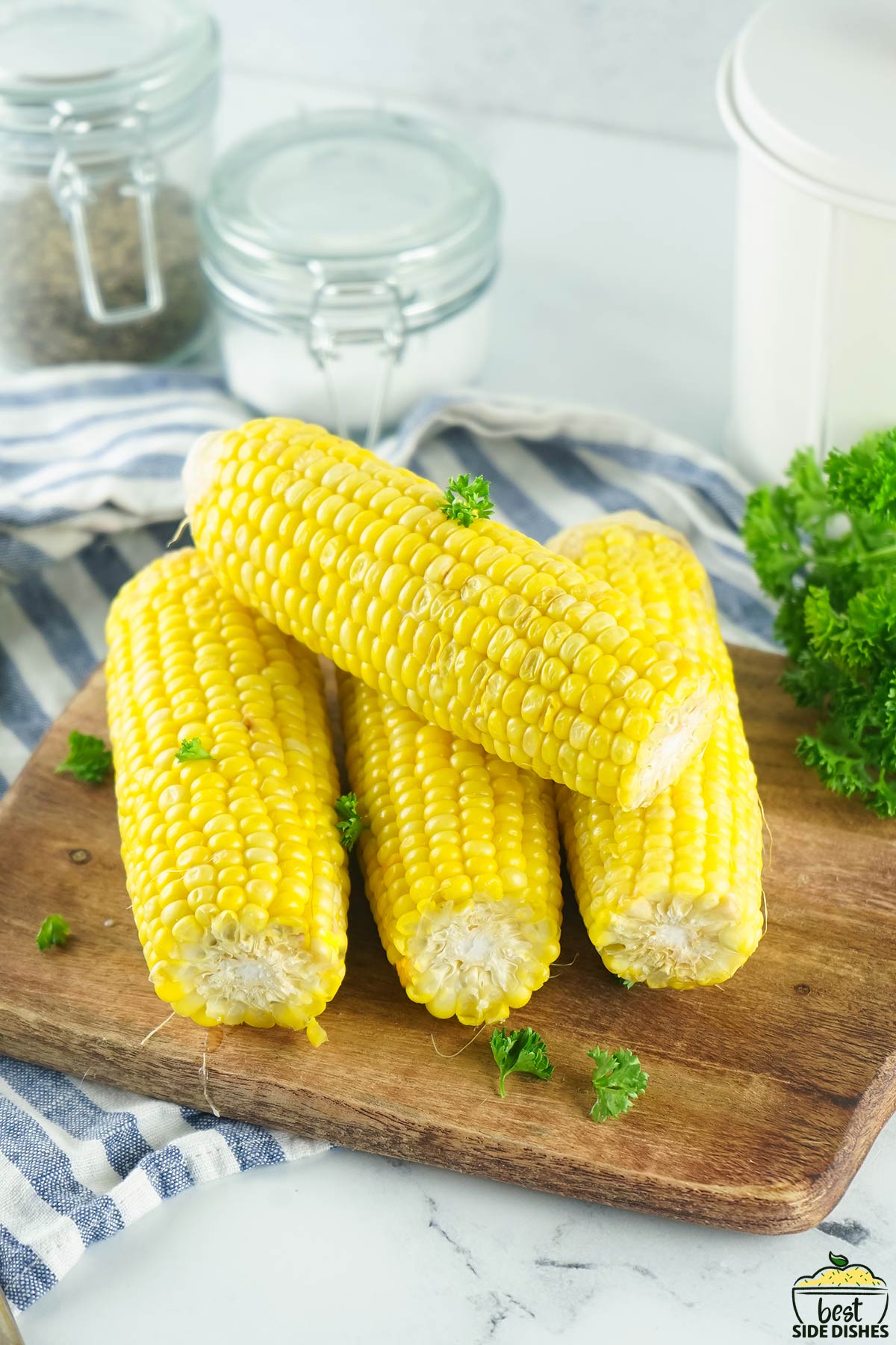 one instant pot corn on the cob stacked on top of three corn on the cob on a wooden board