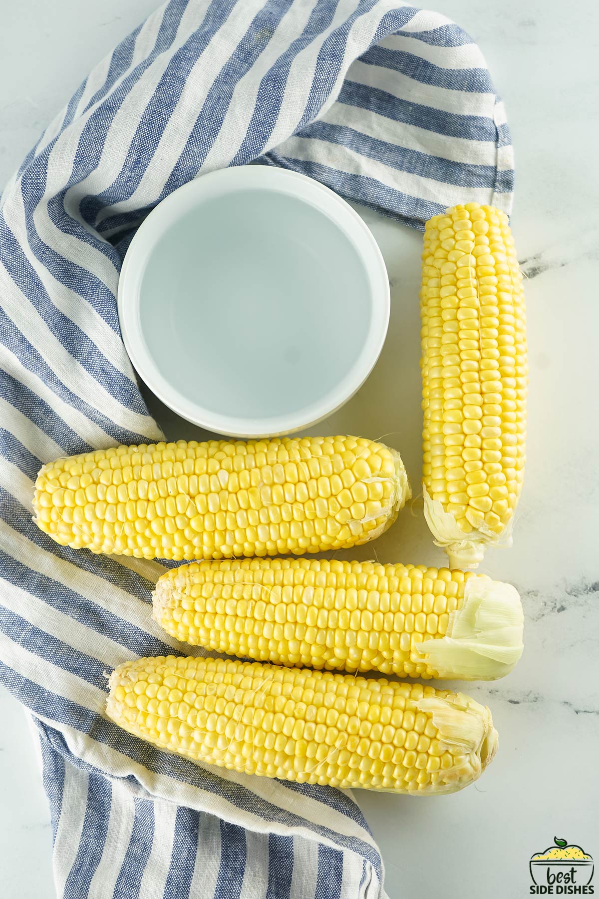 Corn and water for instant pot corn on the cob on a white surface with a towel