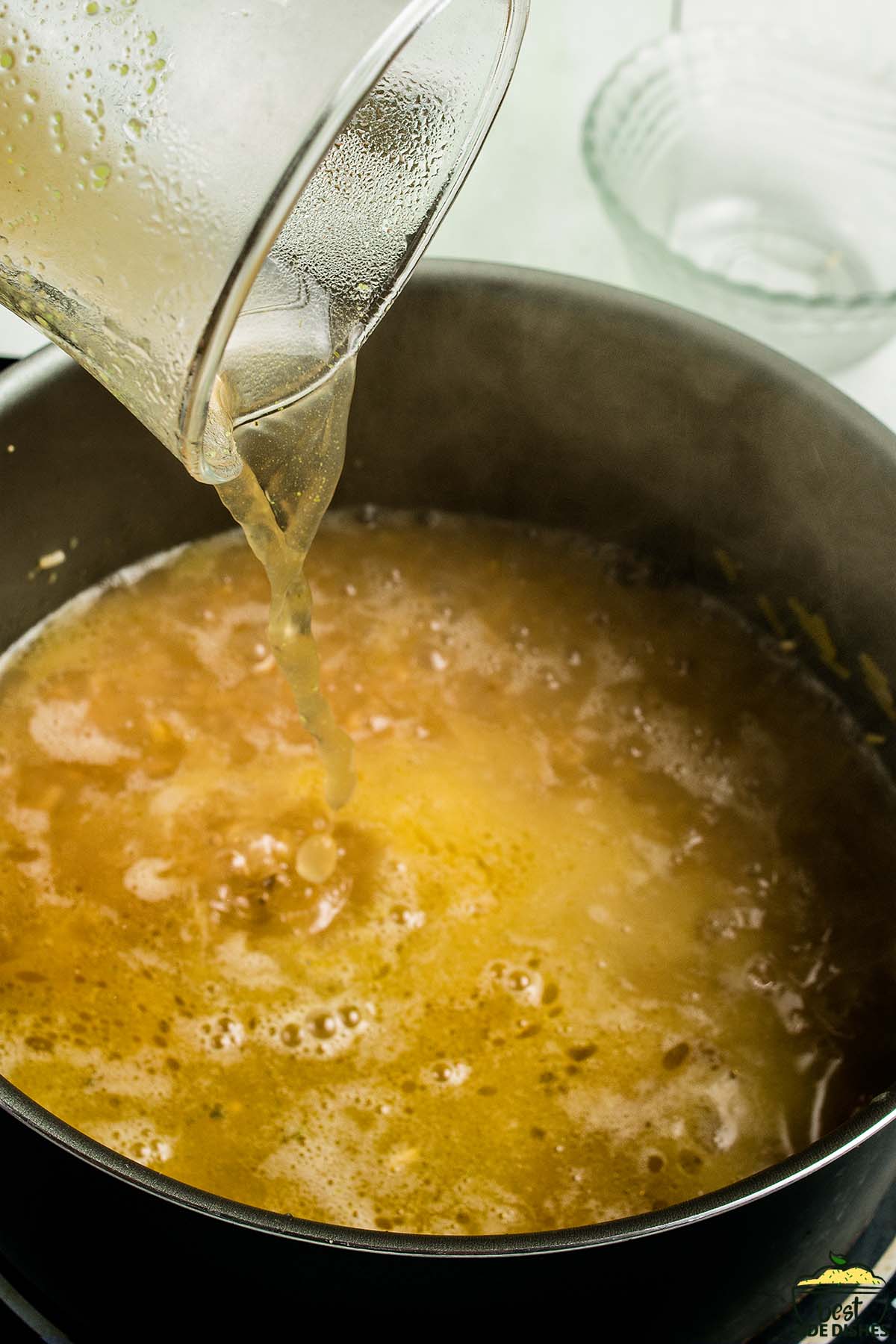 adding chicken stock to a pan