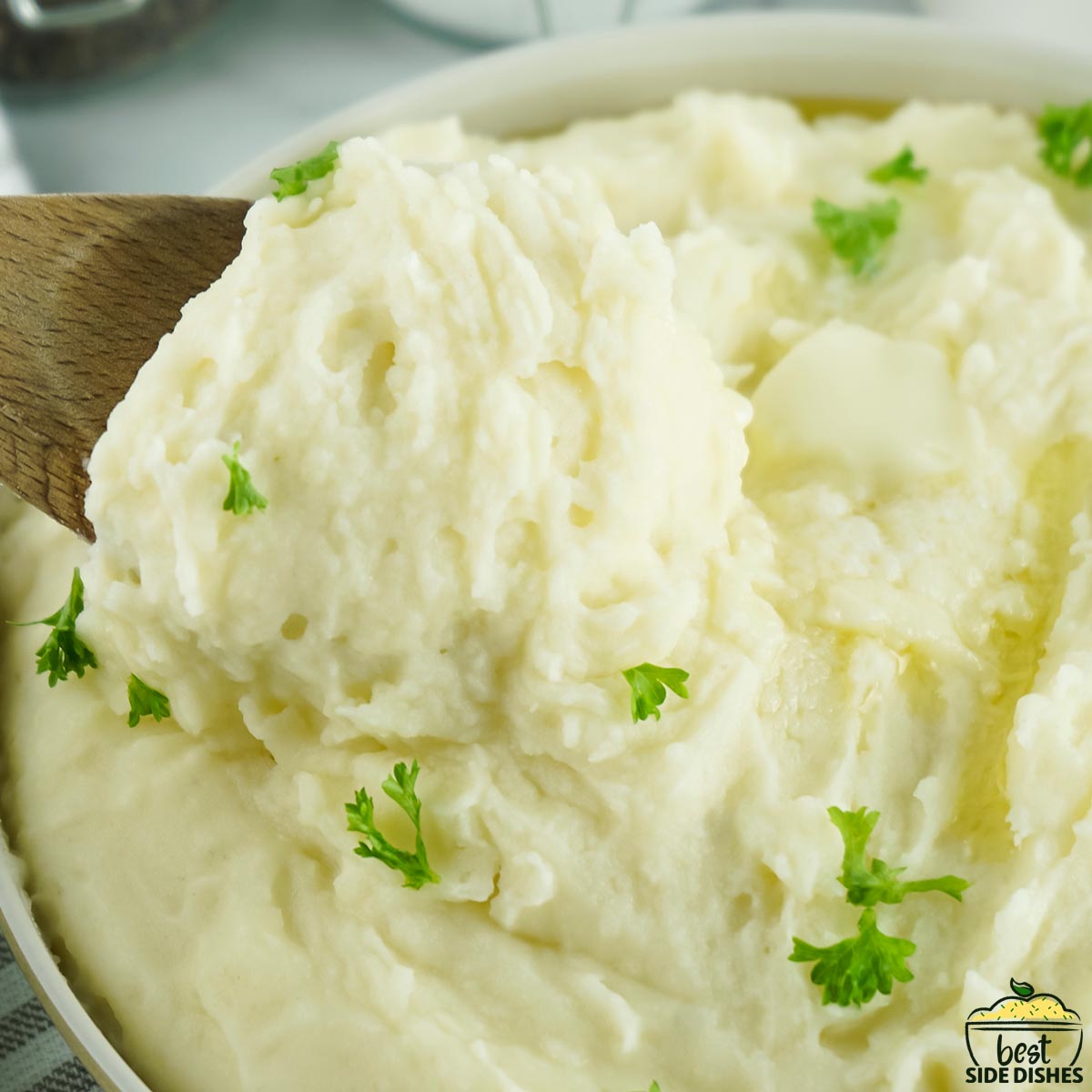 a spoon full of completed mashed potatoes over a serving bowl of mashed potatoes