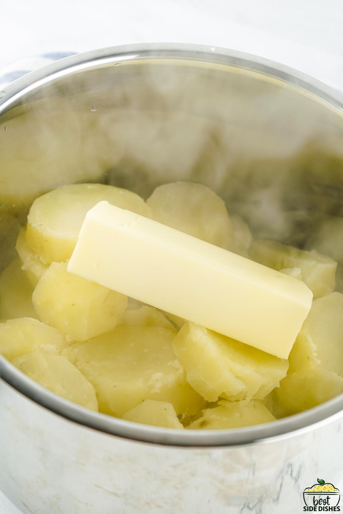 cooked potatoes in a pot with a stick of butter on top