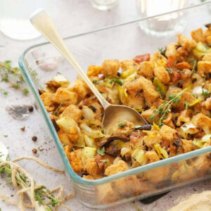 mushroom stuffing in a clear baking dish with a gold spoon inside