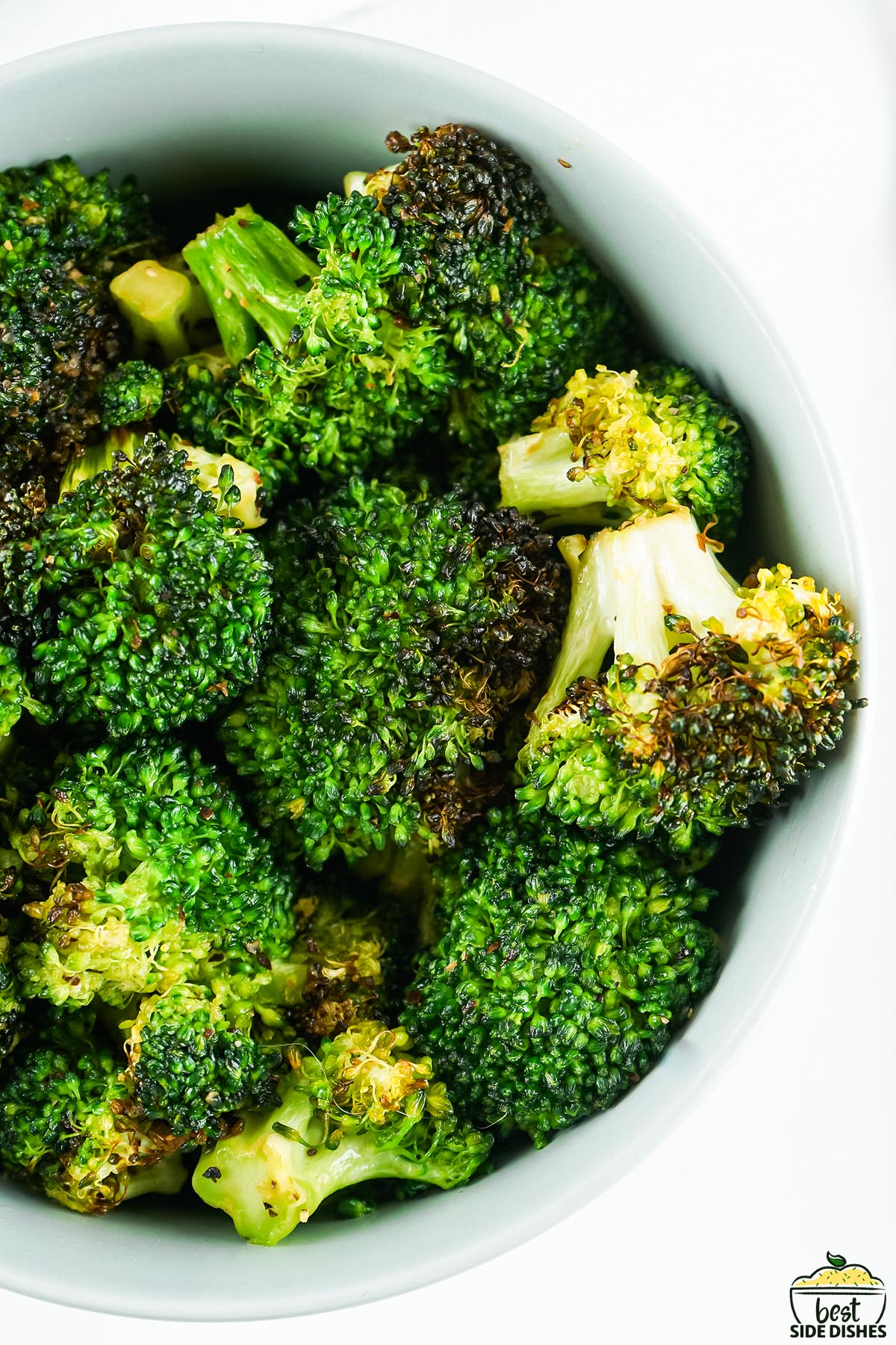 a closeup of cooked broccoli in a white dish on a white background