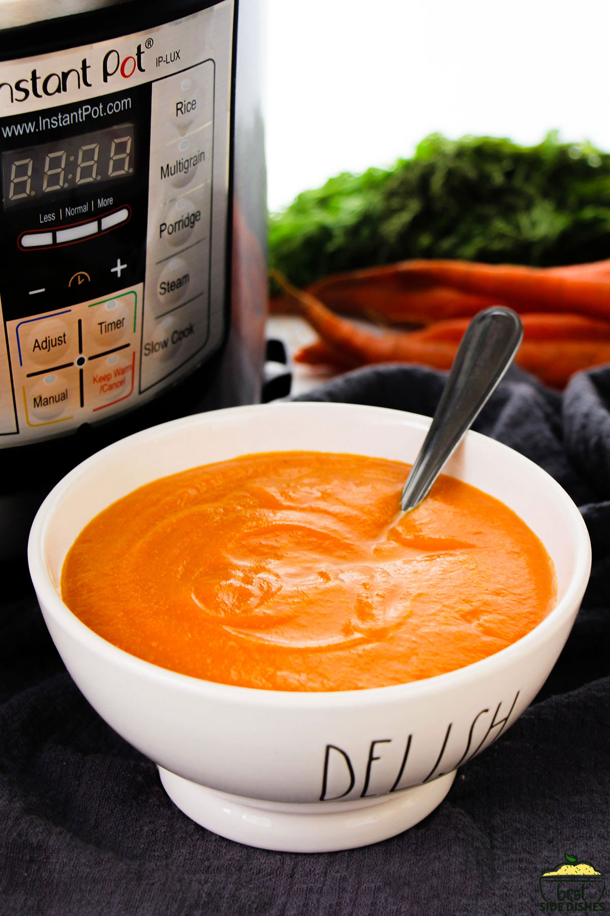 a full bowl of carrot soup next to an instant pot and a bunch of carrots.