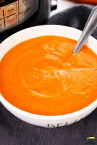carrot soup in a white bowl with a spoon on a grey cloth background