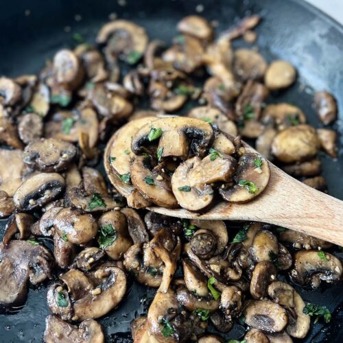 sauteed mushrooms in a pan up close on a wooden spoon