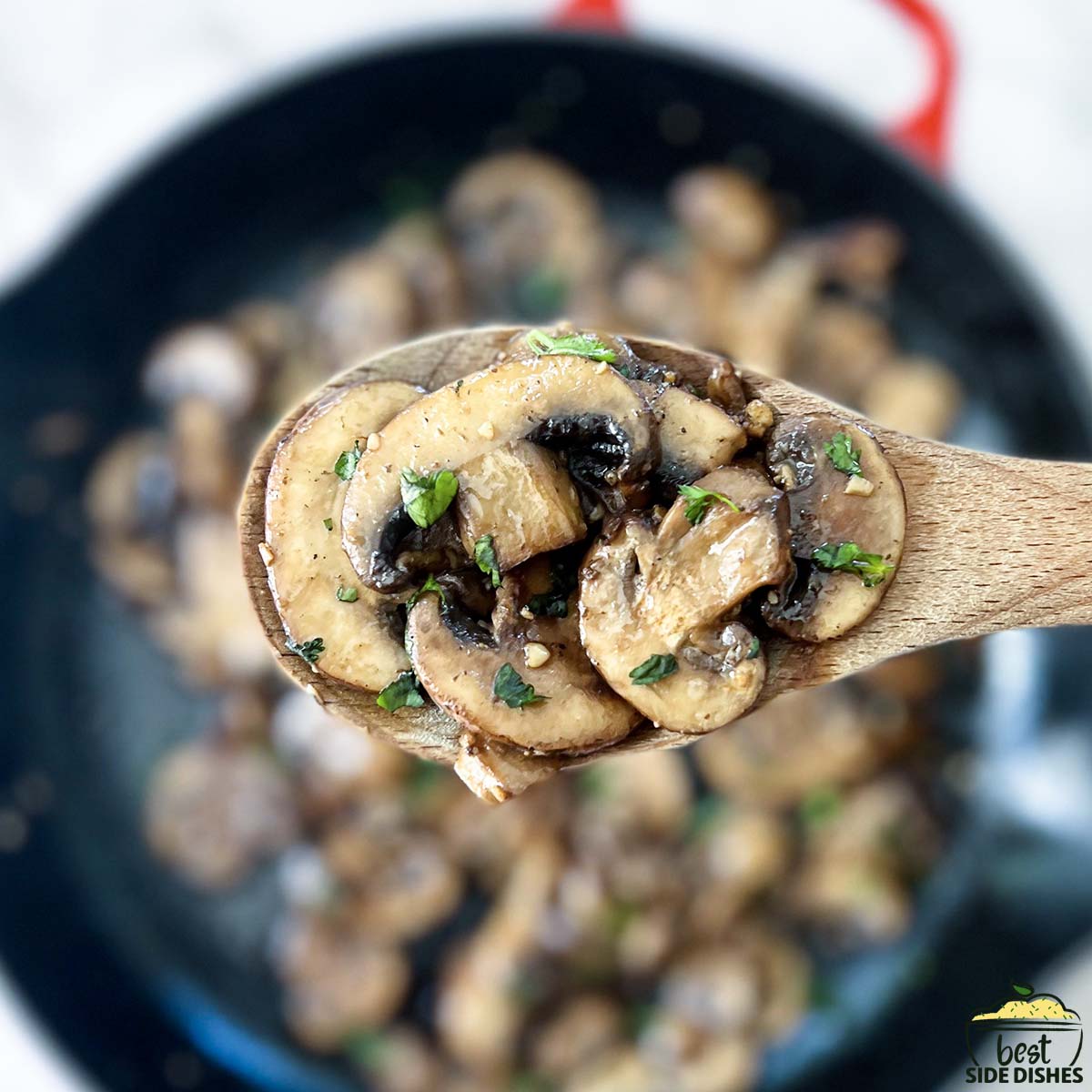 close up of garlic butter mushrooms on a wooden spoon