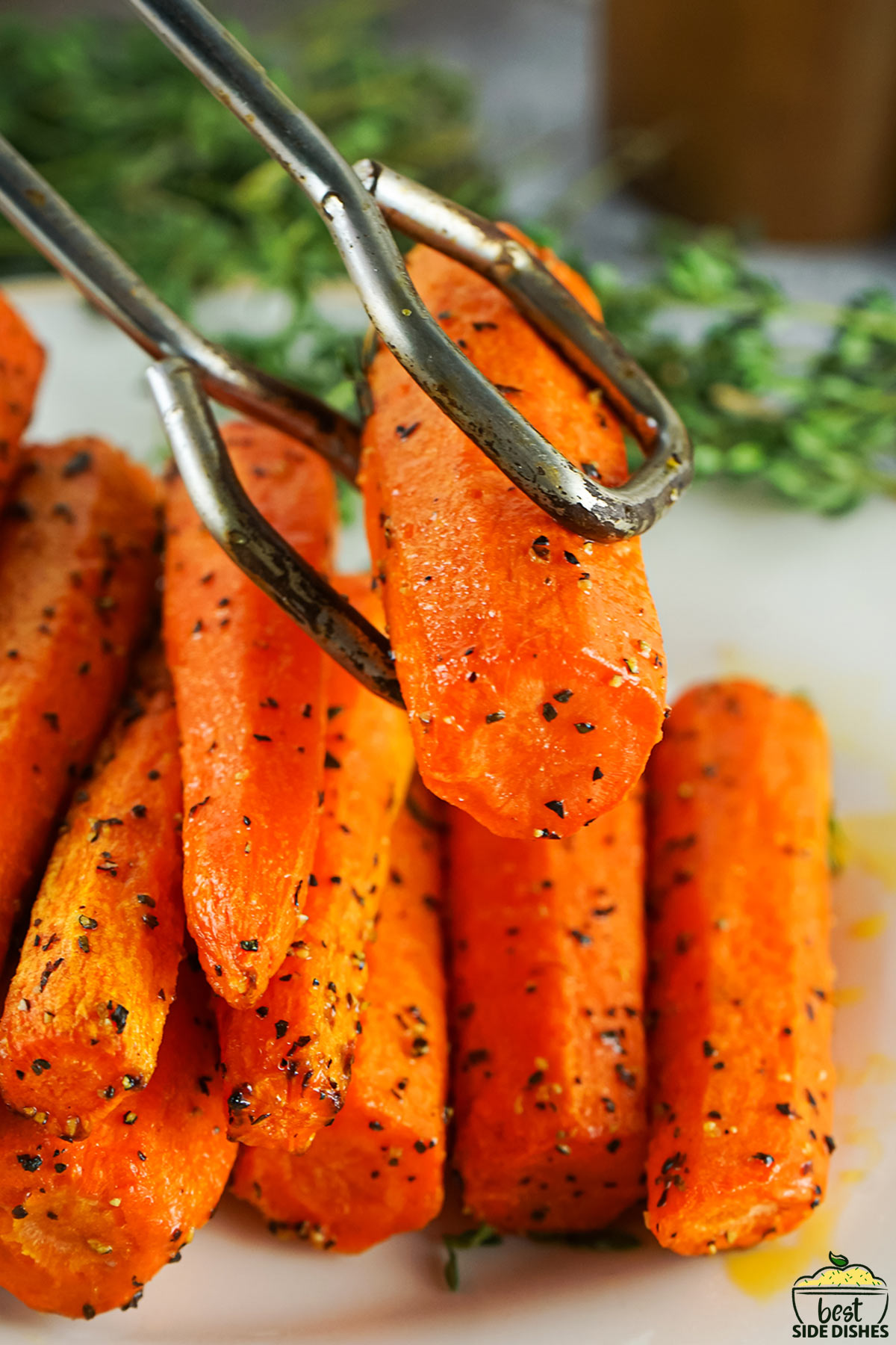 metal tongs holding up a fully cooked air fryer carrot over a plate of carrots