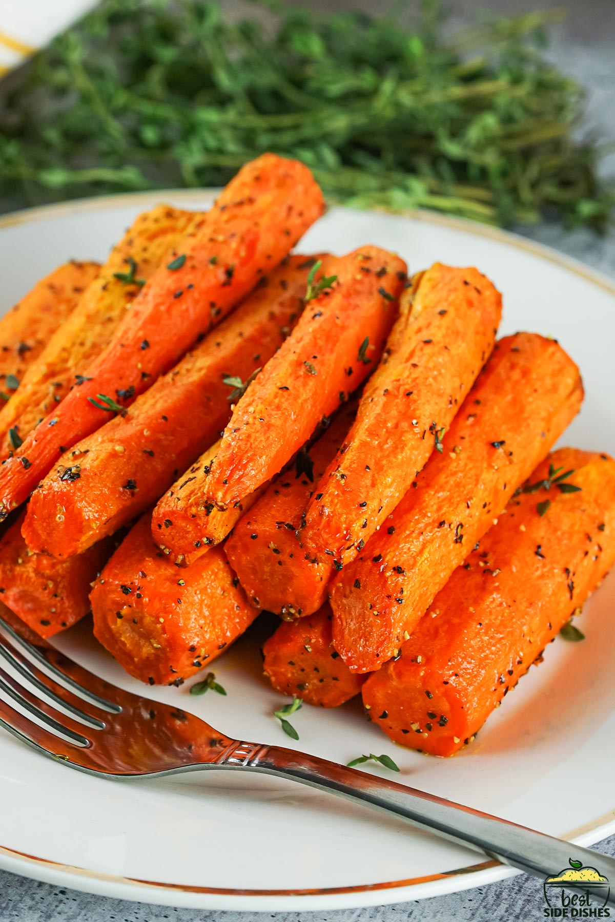 a white plate with a stack of air fryer carrots and a fork, with herbs in the background