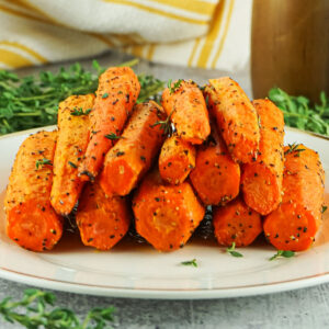 a plate of stacked up air fried carrots with thyme sprigs in the background