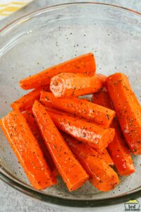 peeled and sliced carrots in a glass bowl coated with oil and seasonings