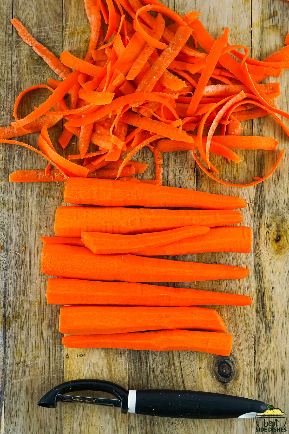 peeled carrots, carrot peels and a carrot peeler on a wooden cutting board