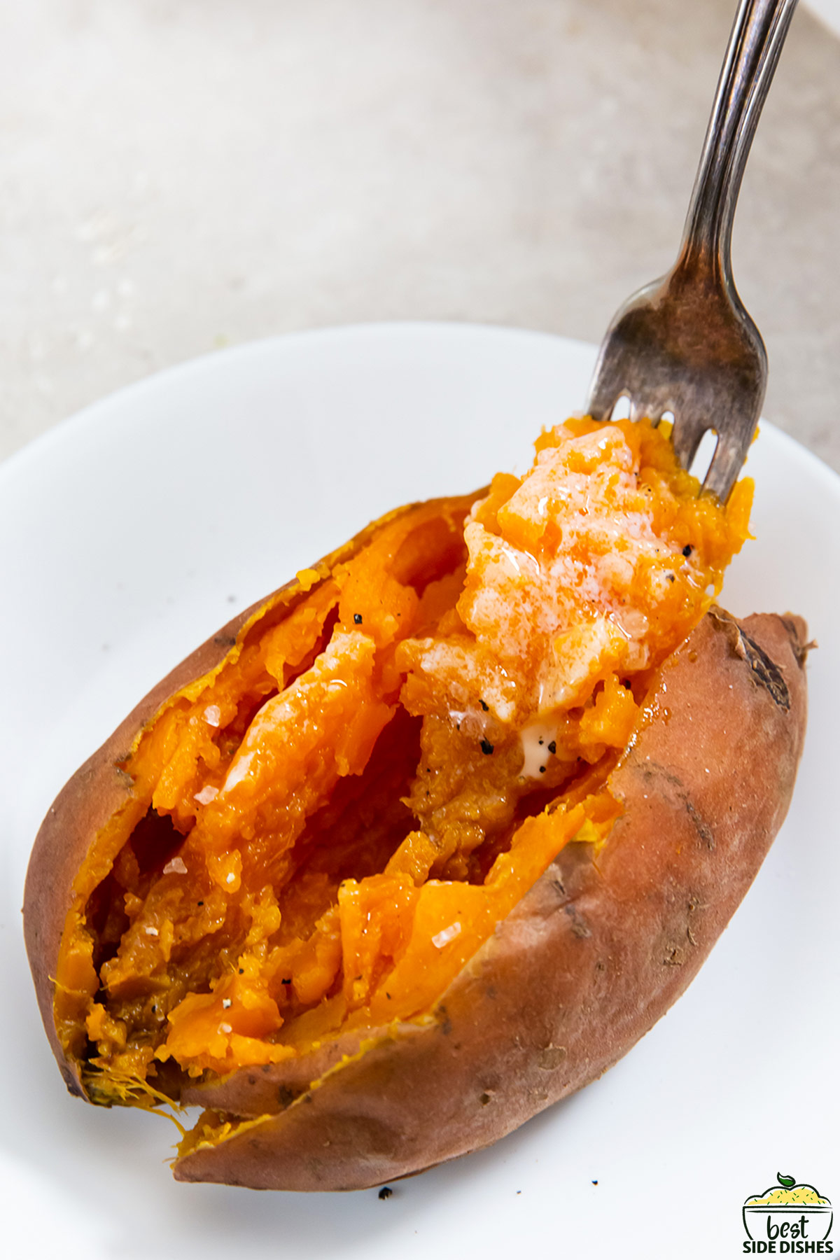 a cooked sweet potato on a white plate with a fork full of sweet potato stuck into it