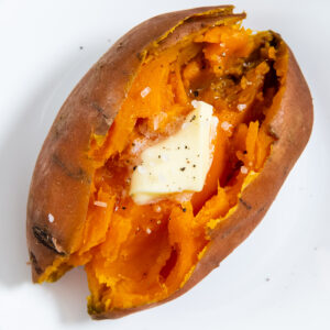 a closeup of a cooked sweet potato cut open with butter, salt and pepper