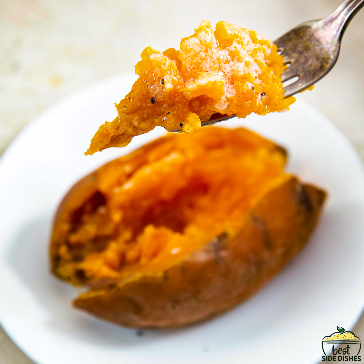 a fork scooping out cooked, buttery sweet potato over a plate with a cooked sweet potato