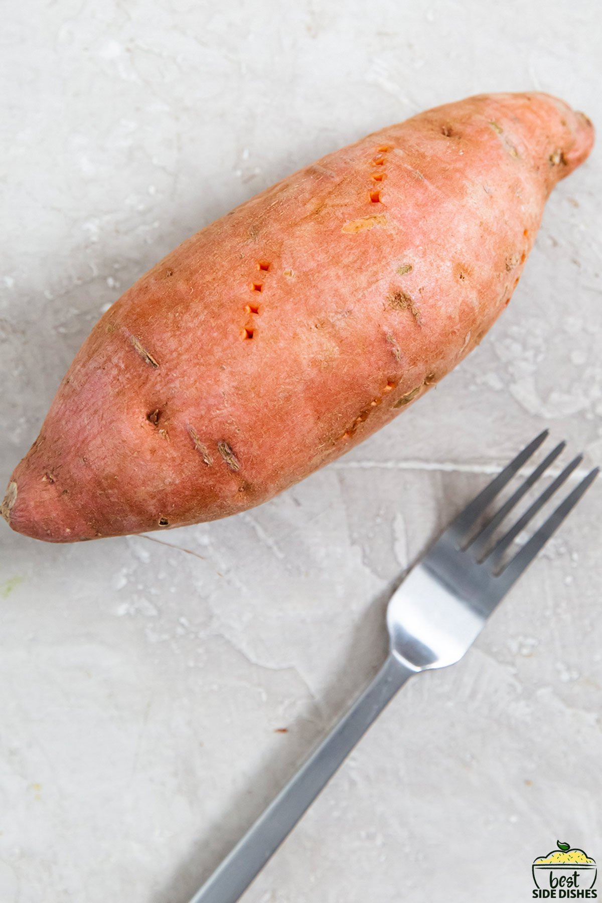 a raw sweet potato on a counter after being pierced with a fork, next to a fork