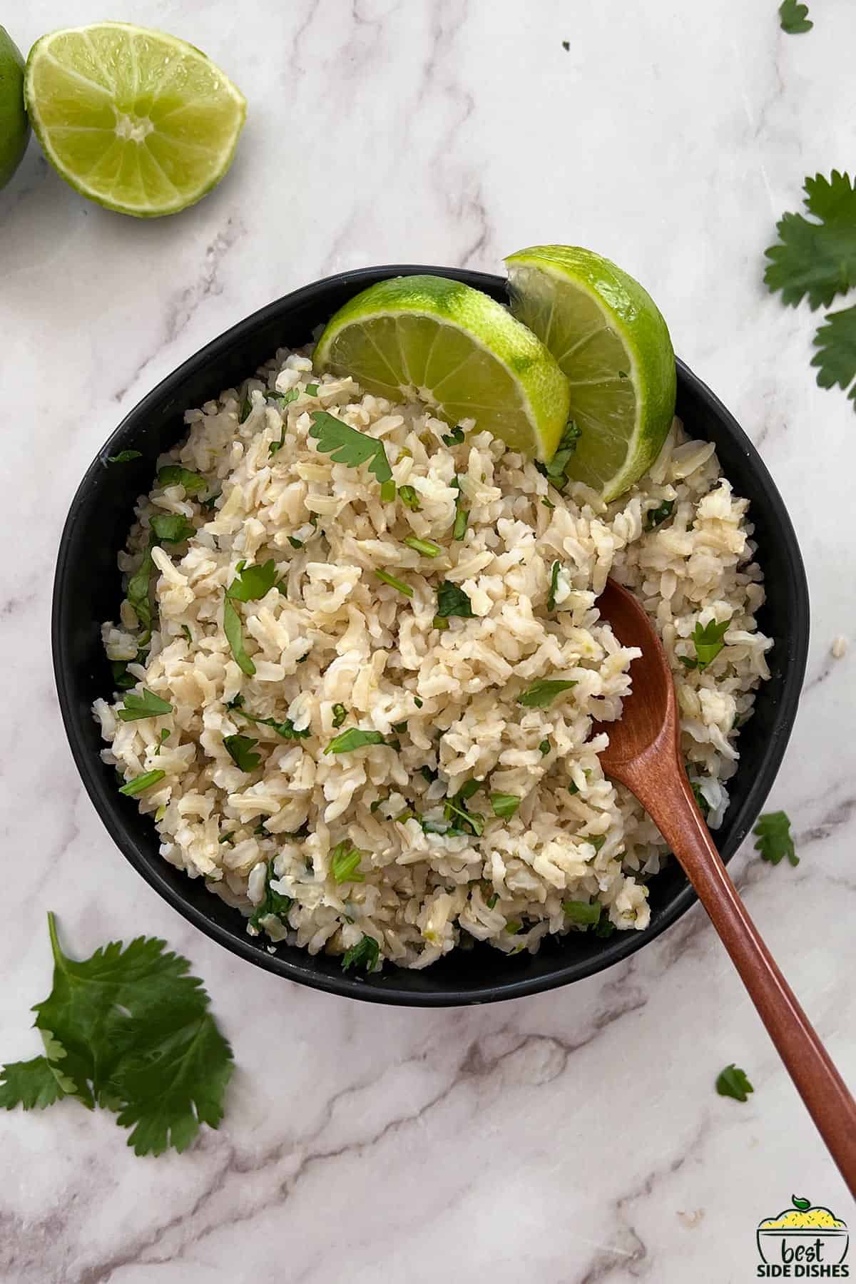 cilantro lime rice in a black bowl with a wooden spoon and lime wedges