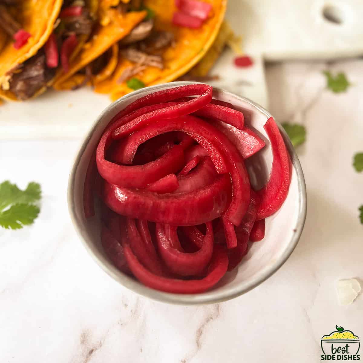 red pickled onions in a small bowl with tacos behind