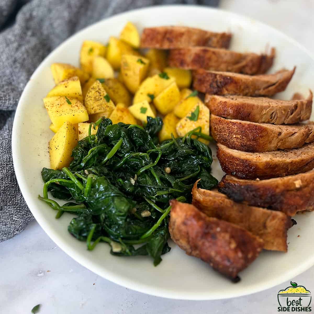 sautéed spinach on a white plate with sliced pork and potatoes