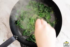 seasoning sautéed spinach in a skillet