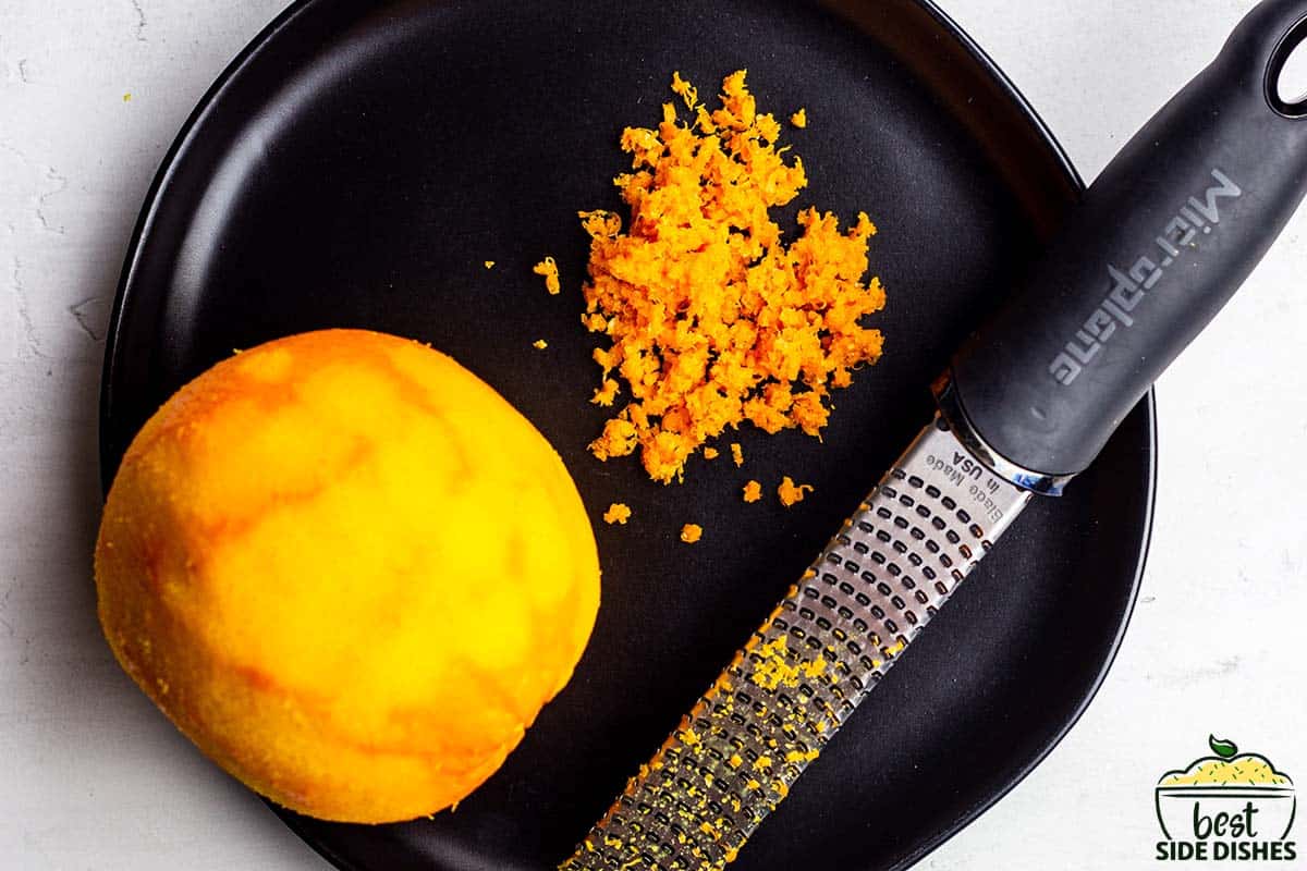 orange and orange zest on a black plate with the grater on the plate