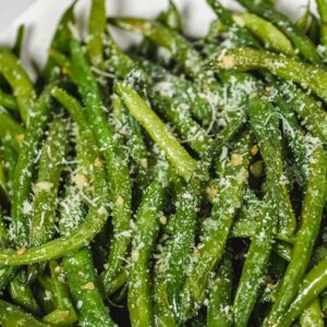 a detail shot of pressure cooker green beans on a white plate covered in garlic and parmesan