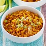 a white bowl filled with Mexican corn casserole next to lime wedges