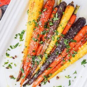 roast carrots on a white platter with parmesan cheese and herbs