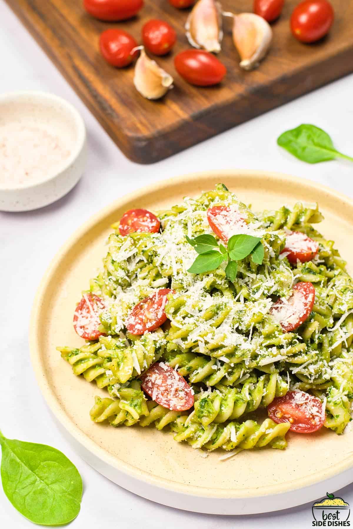 a dinner plate filled with avocado sauce pasta with extra tomatoes in the background