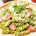 a heaping plate of finished avocado pasta with parmesan, tomatoes, and a basil sprig