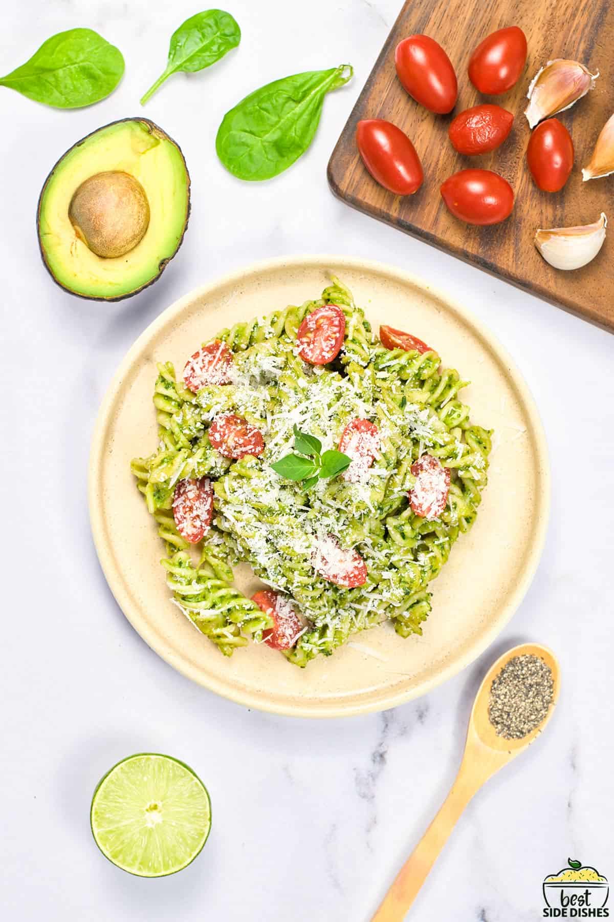 a bowl of completed avocado pasta with extra tomatoes, garlic, avocado, lime, spinach, and pepper.