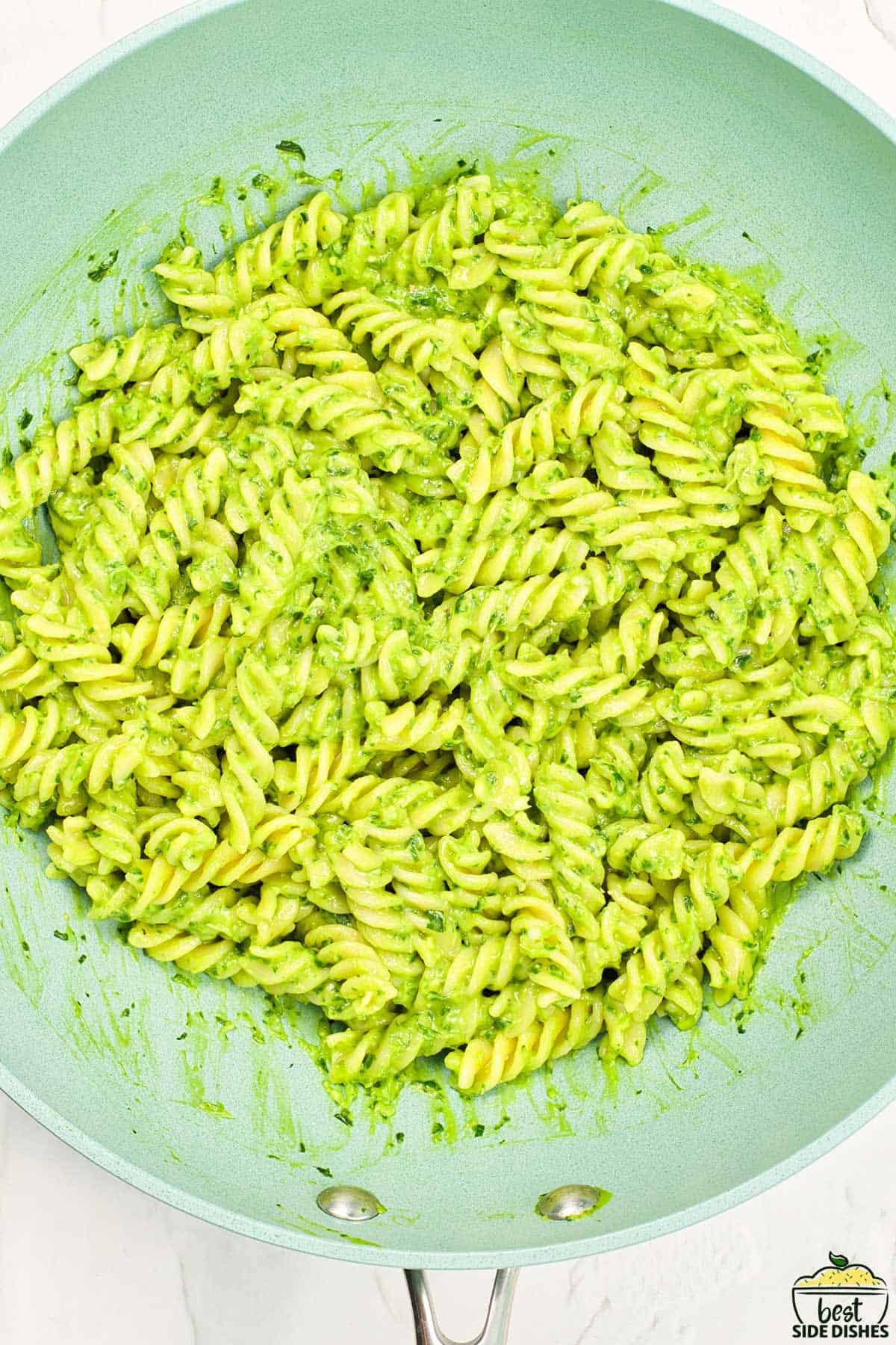avocado sauce in a pan with pasta added in and tossed until coated