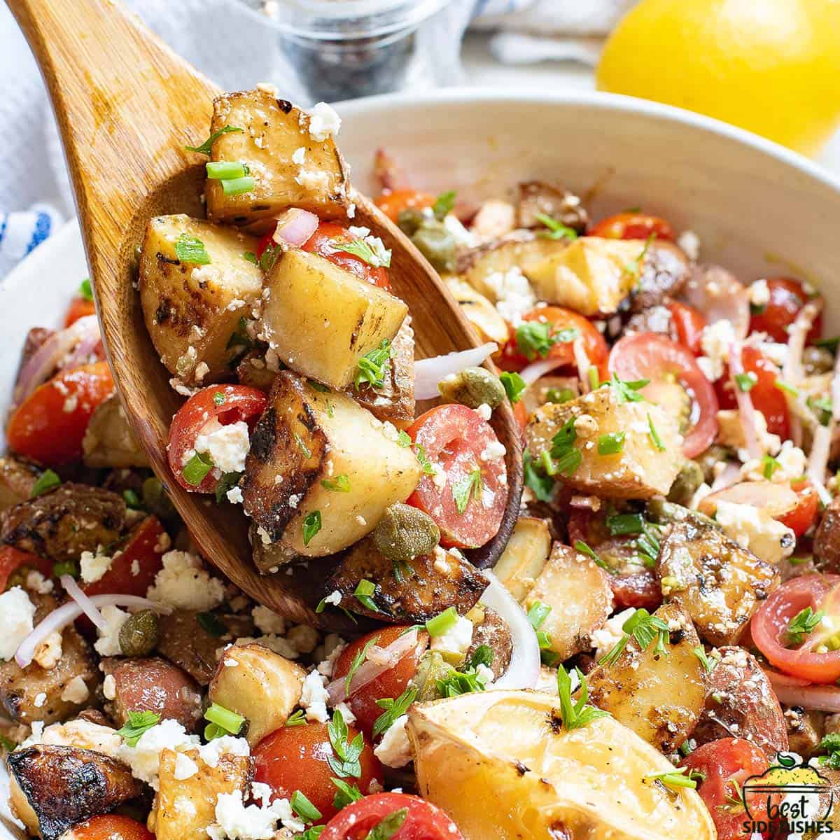 greek potato salad in a white bowl with a wooden spoon