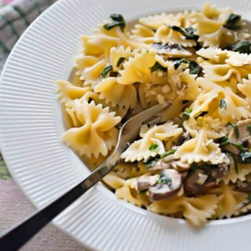 close up of spinach and mushroom pasta in a white deep plate with a fork