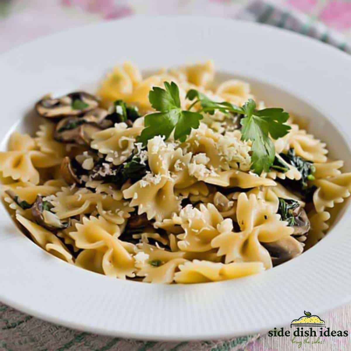 Pasta with spinach and mushrooms topped with parsley and cheese in a white deep plate