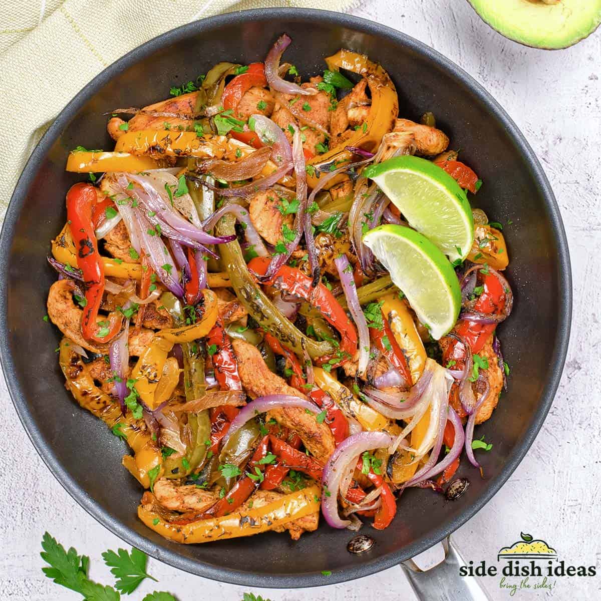 fajita veggies in a skillet with two lime wedges and sliced chicken