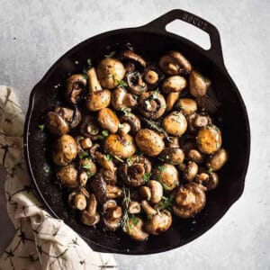 cooked button mushrooms in a skillet with herbs
