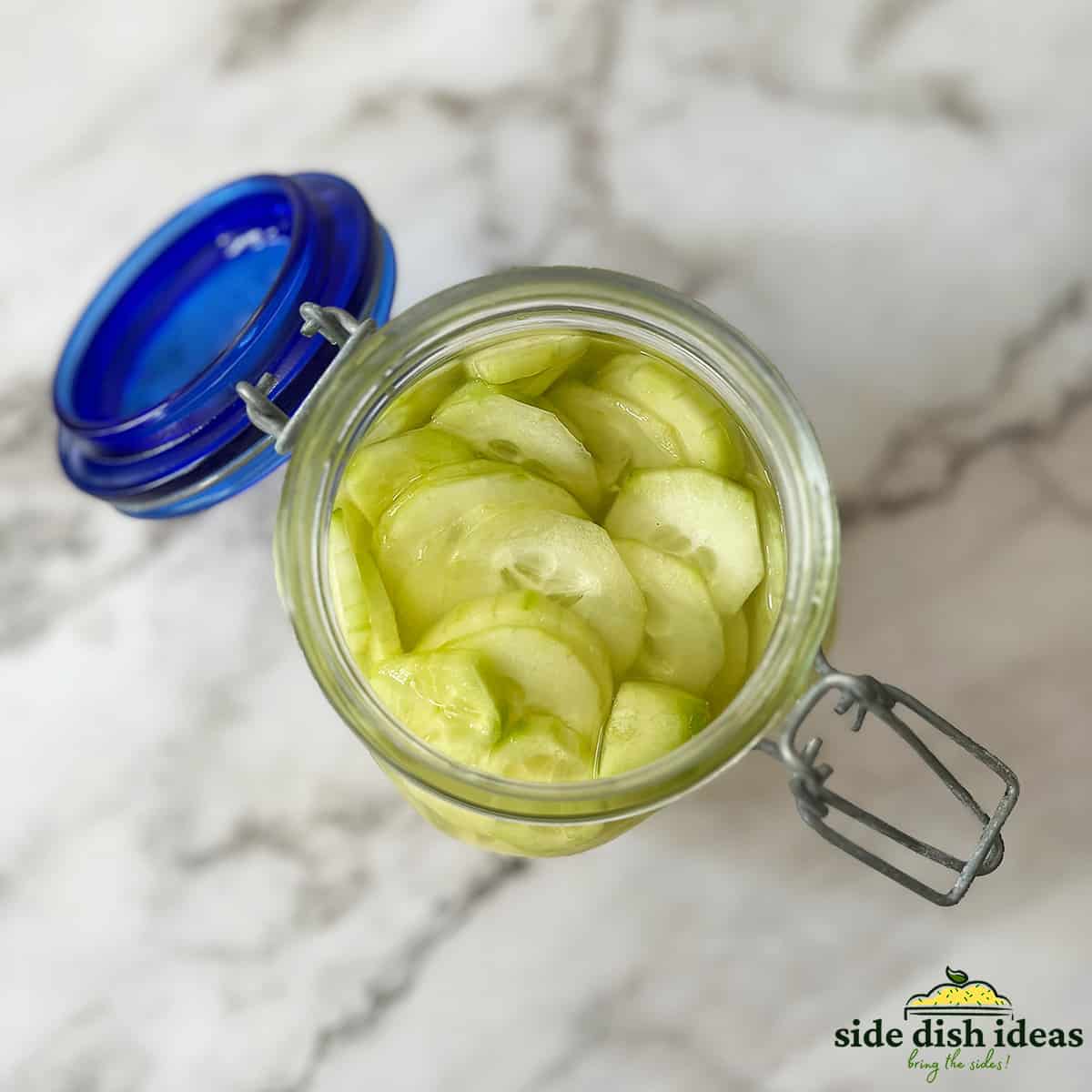 close up of pickled cucumbers inside of a glass jar with an open lid