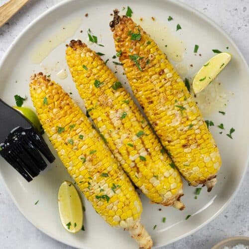 Three corn on the cob pieces on a plate with limes