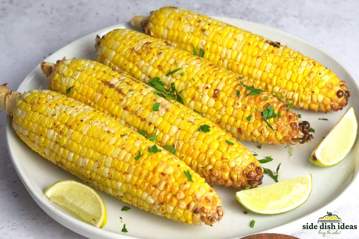 corn on the cob on a white platter with limes