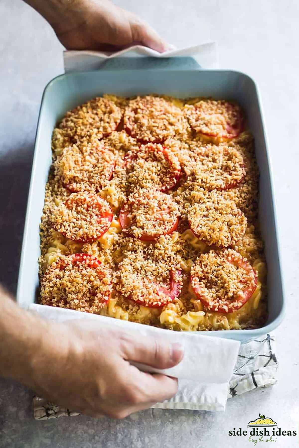 creamy baked mac and cheese in a baking dish topped with breadcrumbs and tomatoes