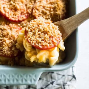 lifting creamy baked mac and cheese out of the dish with a wooden spoon