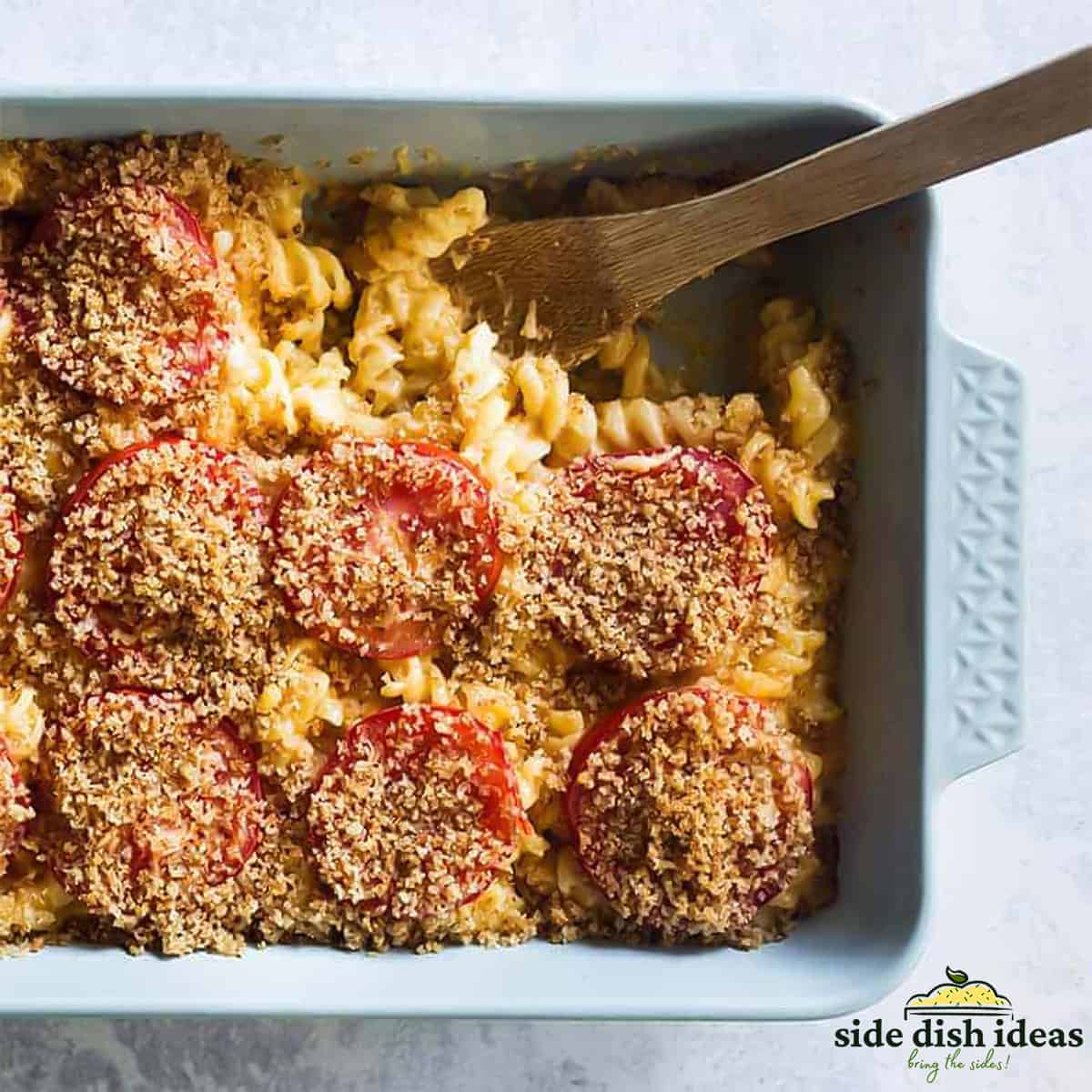 creamy baked mac and cheese in the baking dish topped with tomatoes and breadcrumbs