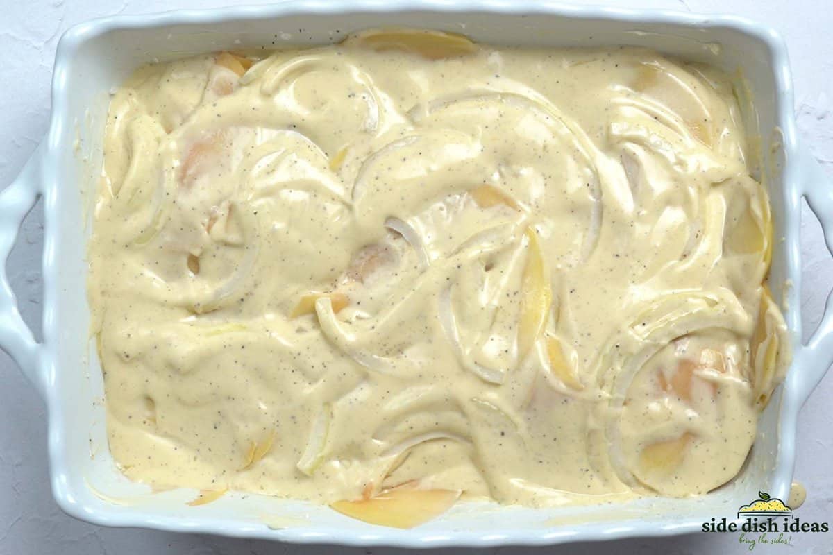 covering potatoes and onions with cheese sauce